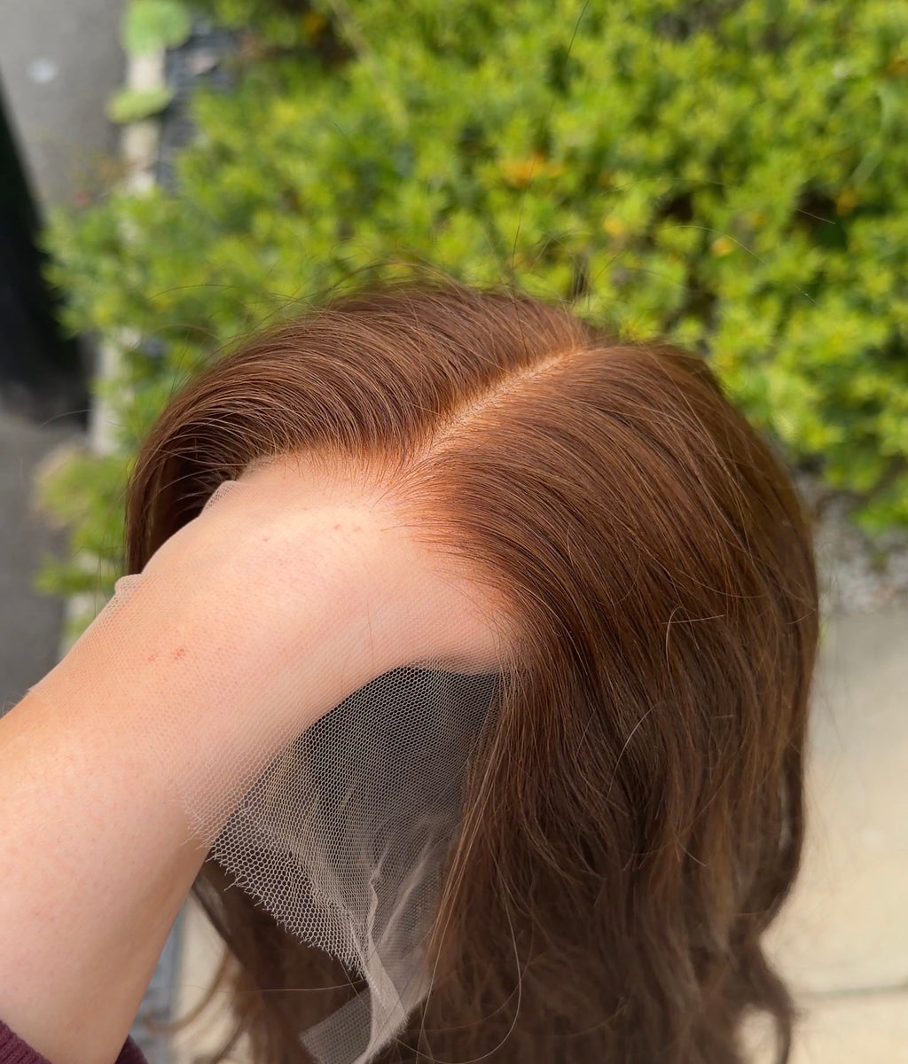 Person holding a brown wig with a blurred green background