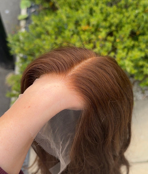 Person holding a brown wig with a blurred green background