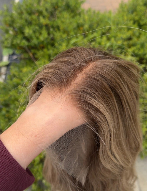 Person holding a blonde wig with a blurred green outdoor background